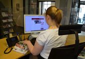 Eine Auszubildende sitzt an einem PC mit einem Stapel Büchern auf der linken Seite