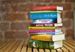 Ein Bücherstapel mit zehn verschiedenen Büchern liegt auf einer Holzbank