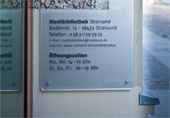 Foto zeigt das Schild mit den Öffnungszeiten, welches am Eingang zur Stadtbibliothek angebracht ist.