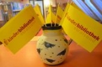 Eine Vase gefüllt mit gelben Fähnchen, die das Logo der Kinderbibliothek Stralsunds in roter Schrift tragen