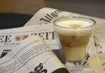 Ein kleines Glas mit Kaffee steht auf einem Stapel verschiedener Zeitungen