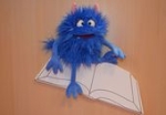 Ein blaues Monster sitzt auf einem Buch und grinst