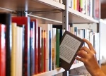 Eine Hand zieht ein eBook-Reader aus einem Bücherregal