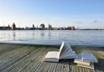 Bücher liegen offen auf einem Steg am Strelasund mit einer Silhoutte von Stralsund im Hintergrund.